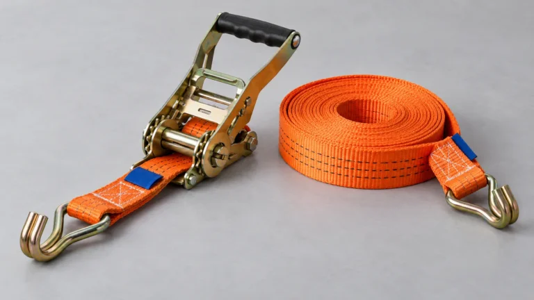 Orange ratchet tie-down webbing with a tensioner and double J hooks on a grey tabletop